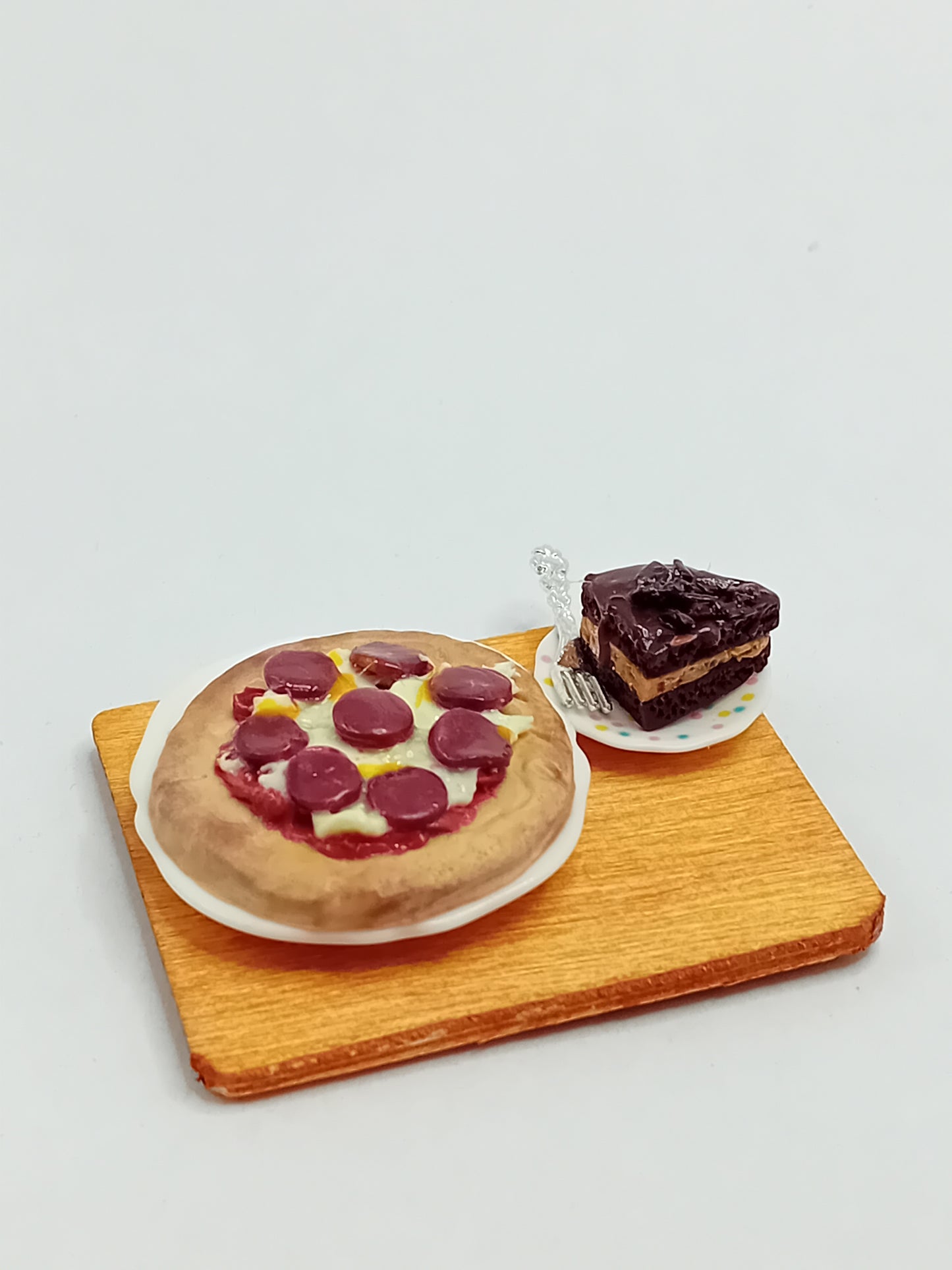 1:12 Scale pepperoni and cheese pizza made from polymer clay on a plate with a side large slice of chocolate cake and silver fork placed on a 5cm x 4cm display board.