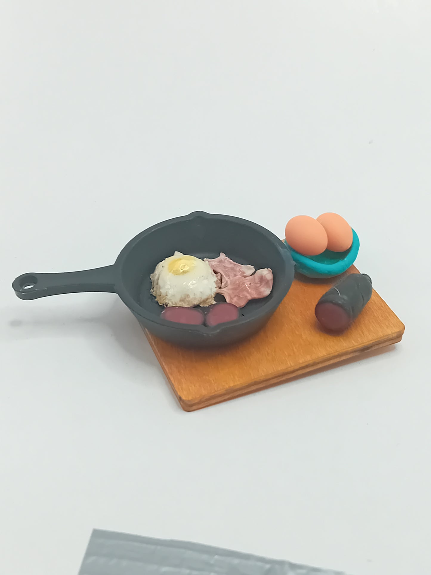 1:12 scale bacon, black pudding & fried egg in a black frying pan placed on a wooden display 5cmx 4cm board.