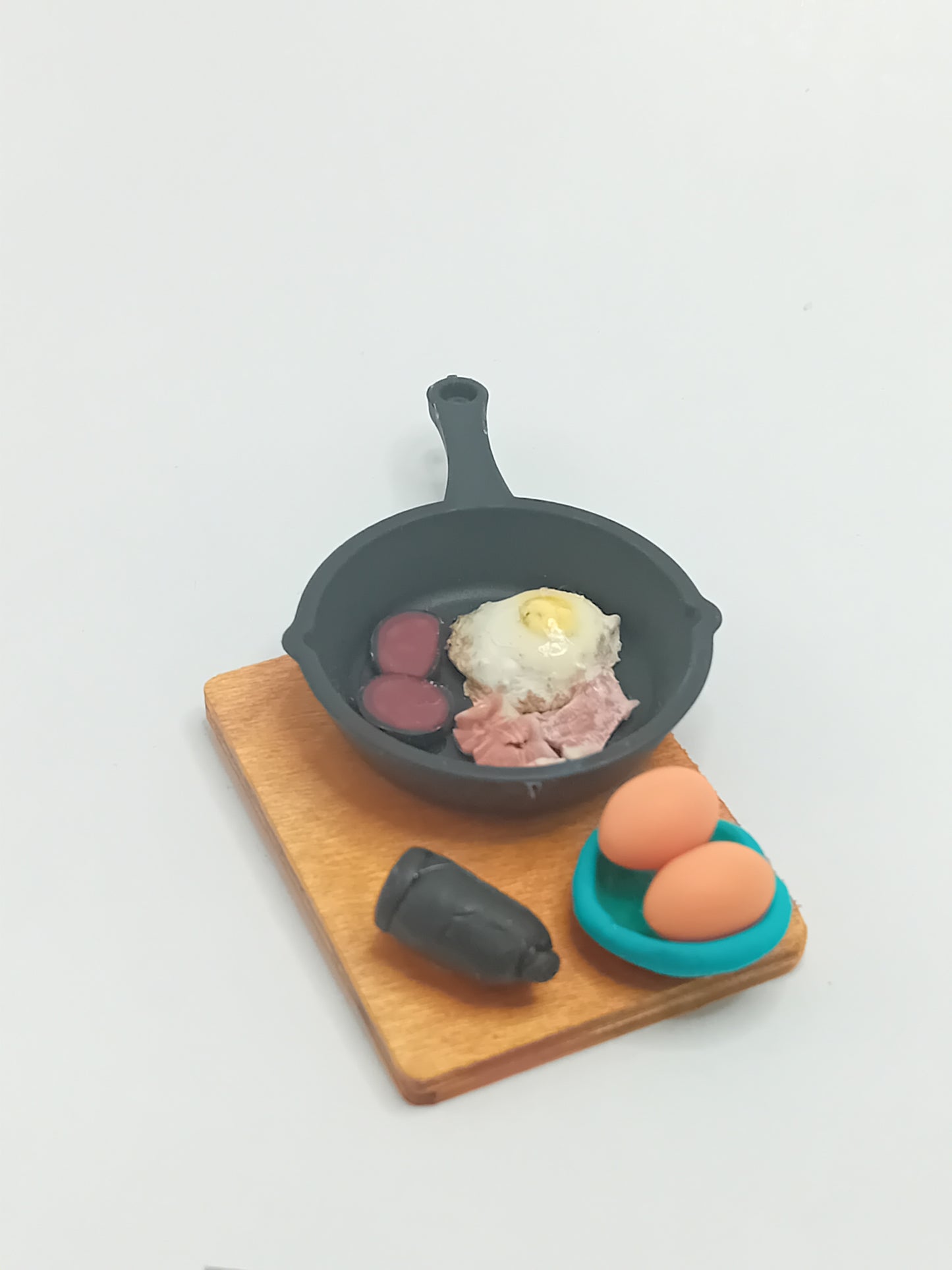 1:12 scale bacon, black pudding & fried egg in a black frying pan placed on a wooden display 5cmx 4cm board.