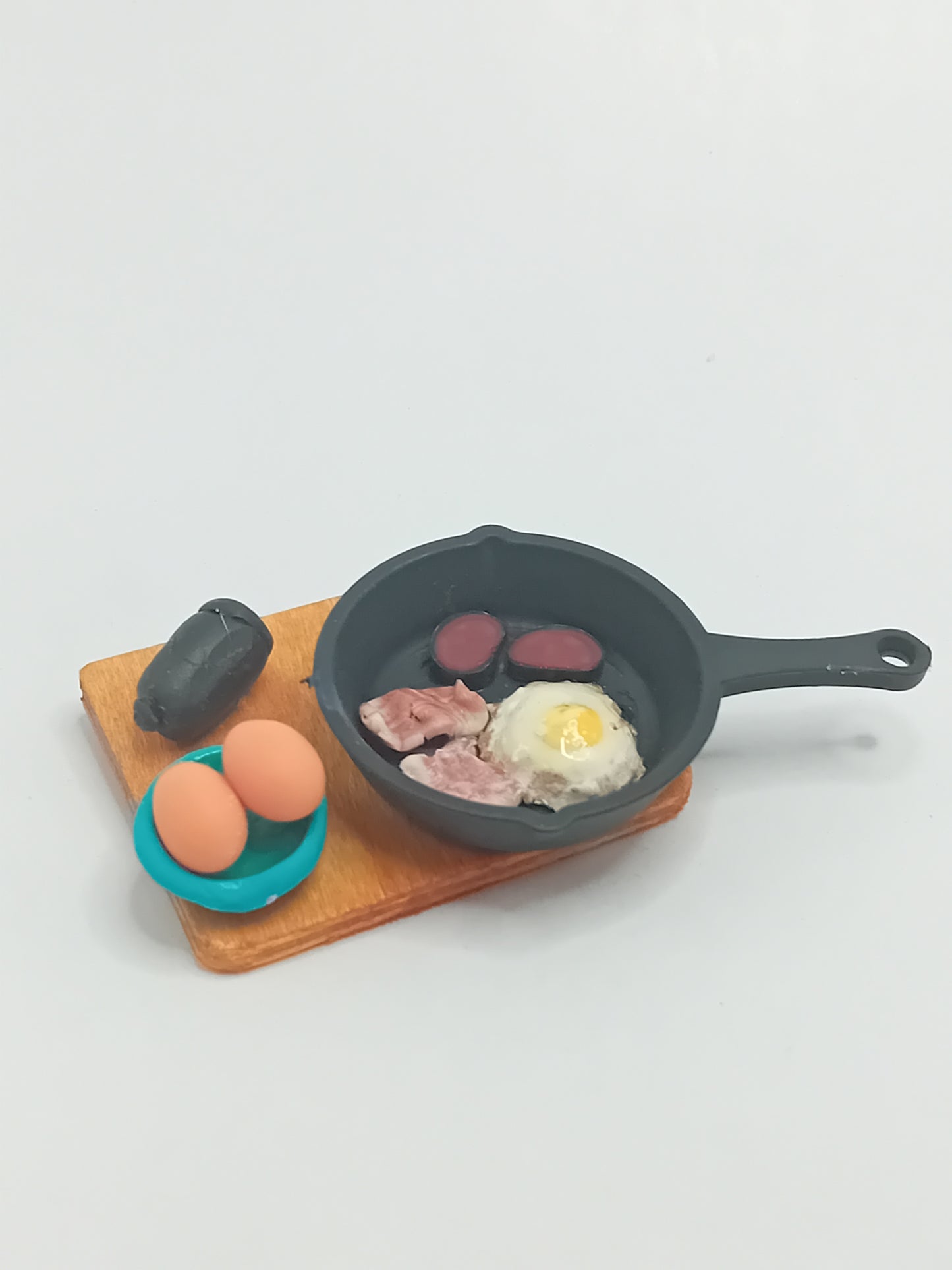 1:12 scale bacon, black pudding & fried egg in a black frying pan placed on a wooden display 5cmx 4cm board.
