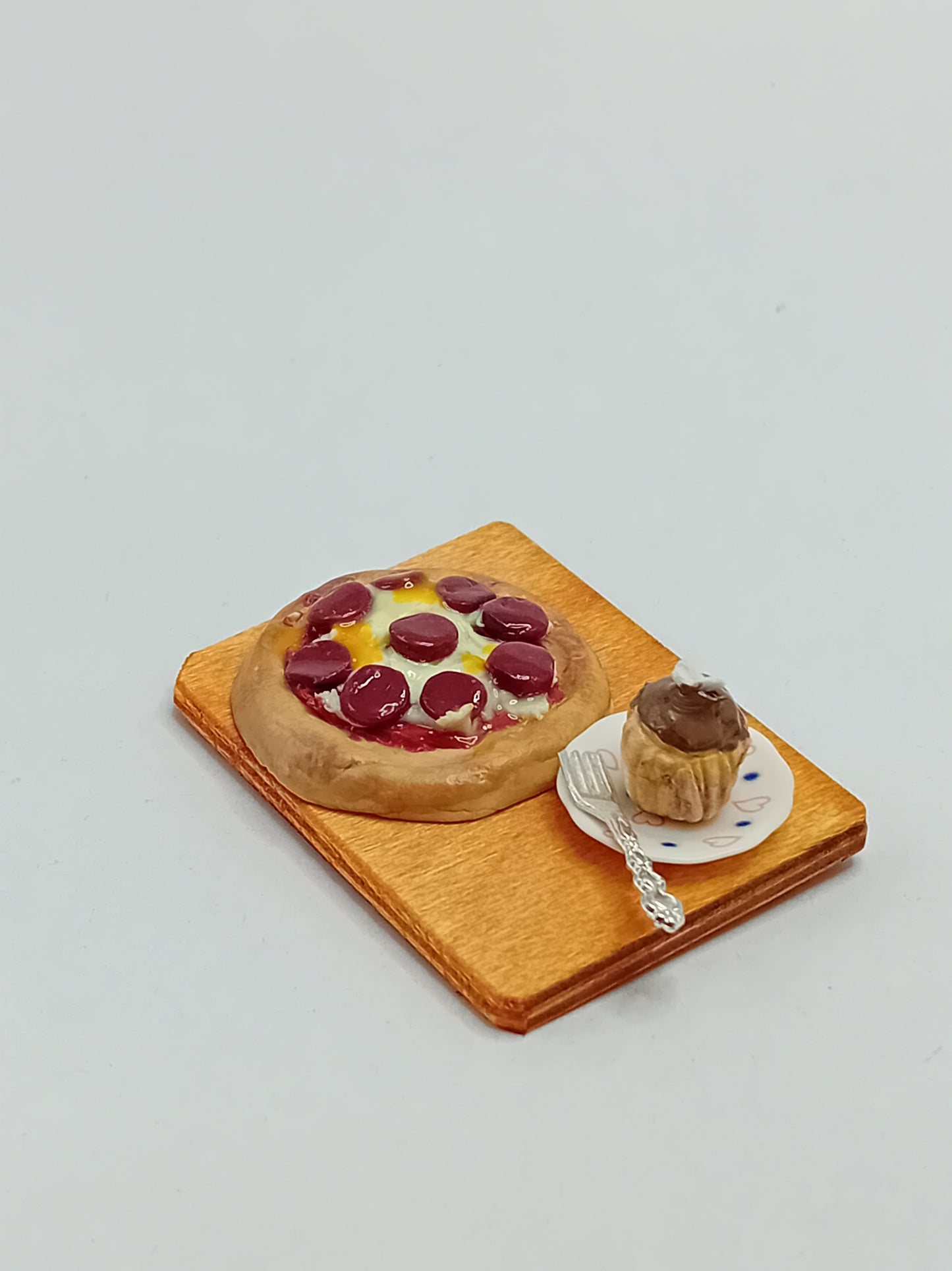 1:12 Scale pepperoni and cheese pizza made from polymer clay on a plate with a side chocolate cupcake and silver fork placed on a 5cm x 4cm display board.