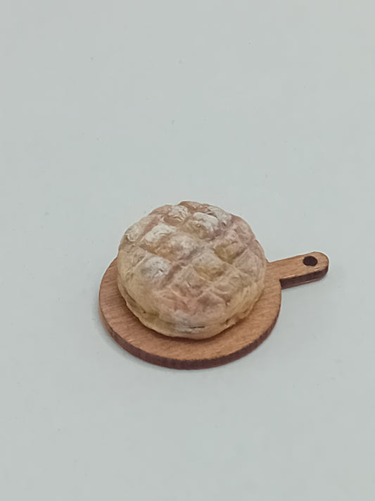 1:12 scale polymer clay rustic sourdough round loaf on a wooden bread board.