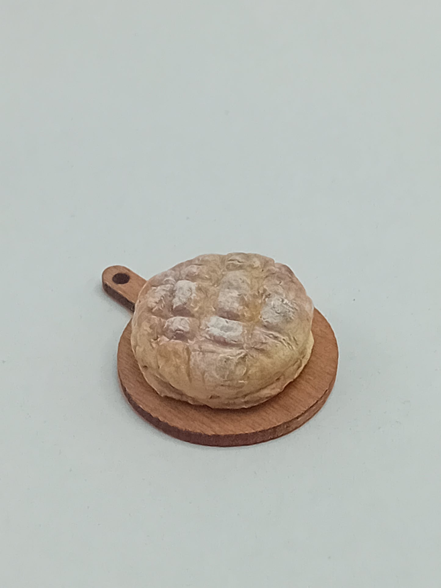 1:12 scale polymer clay rustic sourdough round loaf on a wooden bread board.
