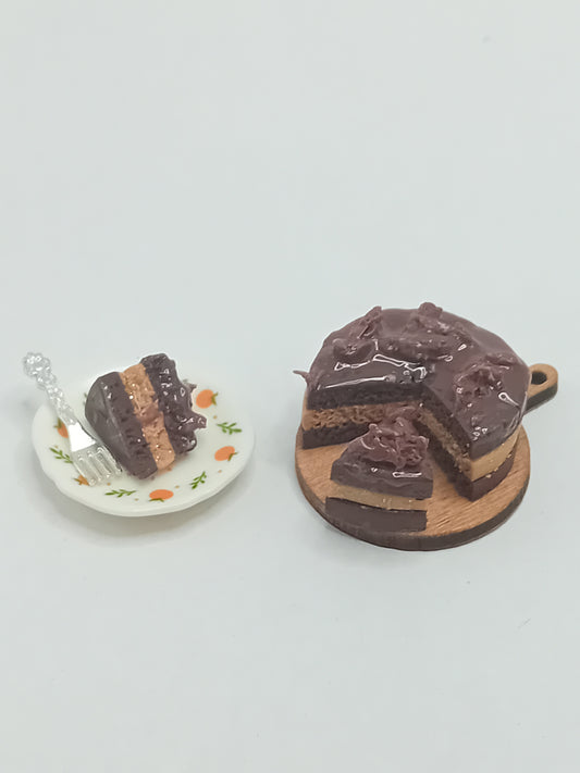 1:12 scale Chocolate Cake on a wooden cake board with a slice on a plate with a silver coloured fork.